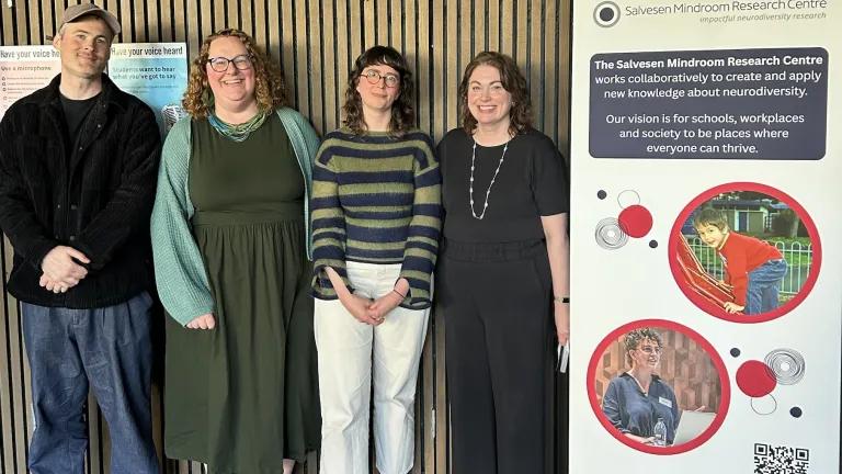 a group of four people standing and smiling next to a research centre banner