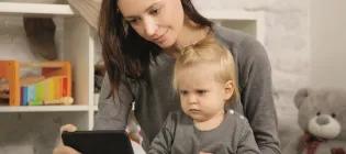 woman looking at a mobile phone with child on her knee