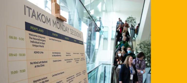 photo of delegates descending on escalator next to conference timetable