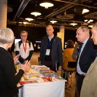 Photo of six people standing chatting around a table with leaflets on it