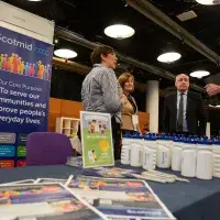 Photo of four people chatting in front of 'ScotMid' poster next to table with leaflets and drinks bottles on top of it