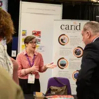 Photo of three people chatting in front of two posters, one of which says 'carid'
