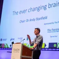 Photo of speaker at lecturn with digital poster behind denoting 'the ever changing brain' title and 'chair: dr andy stanfield'