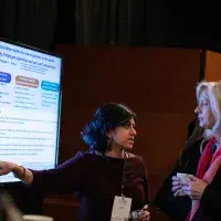 Photo of two females discussing a digital poster on screen