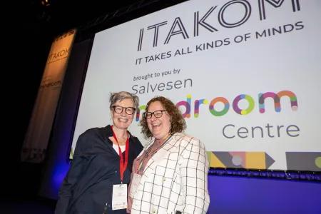 Photo of two ladies standing in front of screen displaying ITAKOM logo and Salvesen Mindroom Centre logo