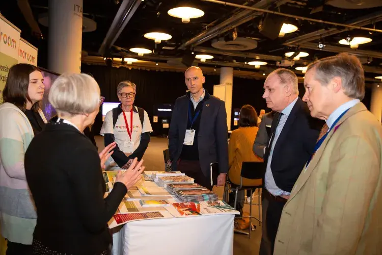 Photo of six people standing chatting around a table with leaflets on it