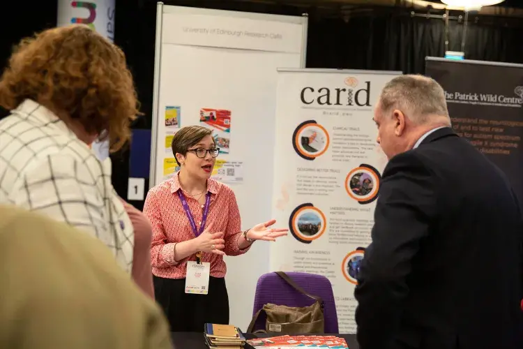 Photo of three people chatting in front of two posters, one of which says 'carid'