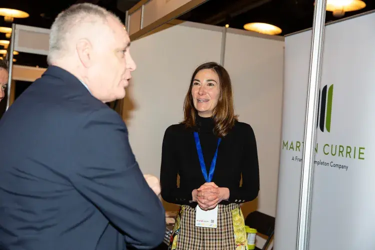 Photo of two people chatting beside a poster with title 'Martin Currie'