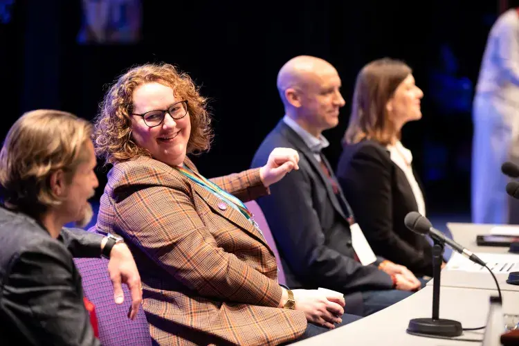 Photo of panel of four people sitting at table with microphone placed on it