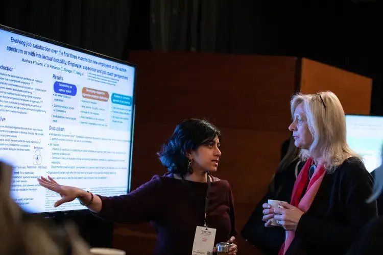 Photo of two females discussing a digital poster on screen